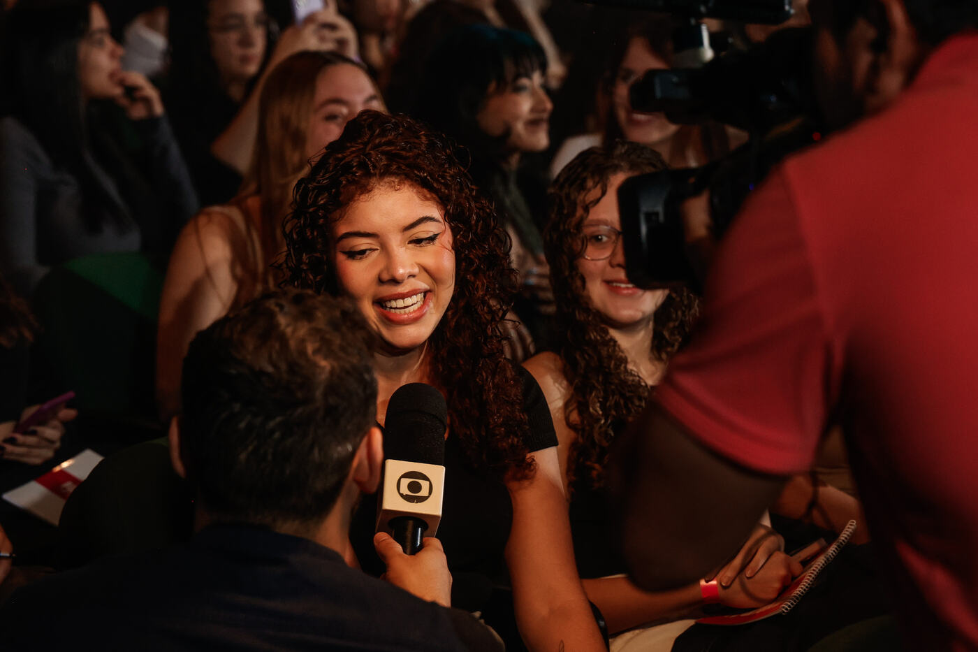 Estudante sorrindo responde ao microfone da Globo na plateia